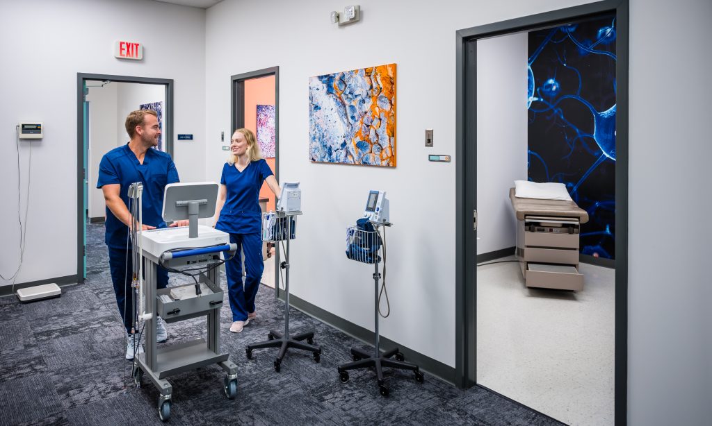 Two employees in scrubs standing in hall outside of patient rooms